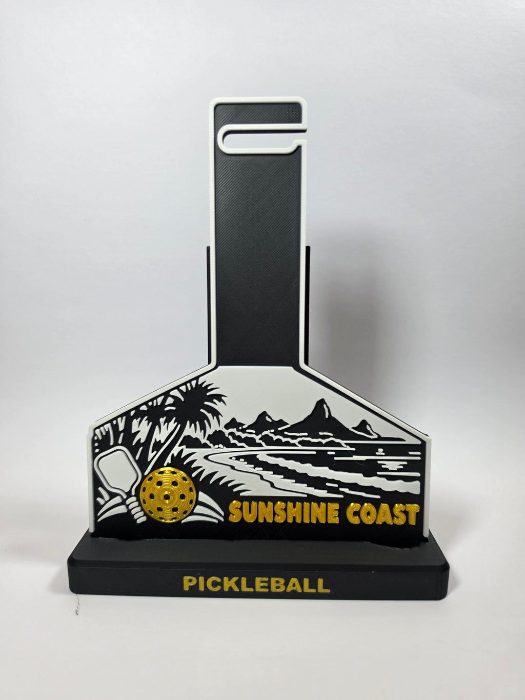 A pickleball-themed decorative plaque or stand with a black and white coastal landscape design, a yellow pickleball graphic, and the words 'SUNSHINE COAST' and 'PICKLEBALL' on a light gray background.