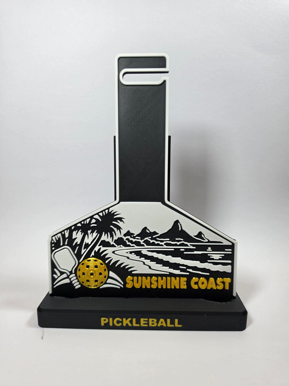 A pickleball-themed decorative plaque or stand with a black and white coastal landscape design, a yellow pickleball graphic, and the words 'SUNSHINE COAST' and 'PICKLEBALL' on a light gray background.