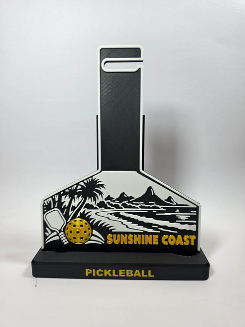 A pickleball-themed decorative plaque or stand with a black and white coastal landscape design, a yellow pickleball graphic, and the words 'SUNSHINE COAST' and 'PICKLEBALL' on a light gray background.