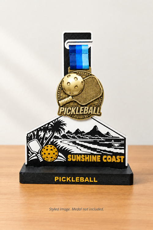 A pickleball-themed commemorative plaque and medal set on a black base. The plaque features a black-and-white beach scene with palm trees, mountains, and a pickleball, with the text 'SUNSHINE COAST.